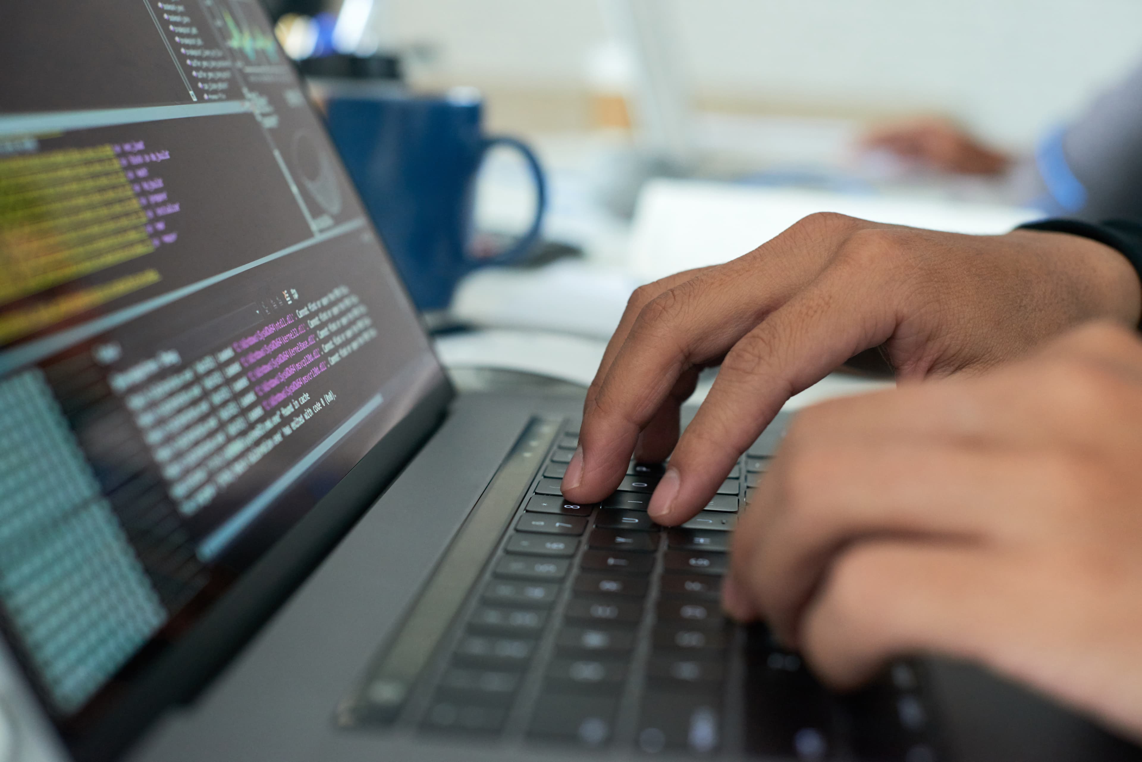 Manos escribiendo código en un portátil, pantalla con un editor de desarrollo